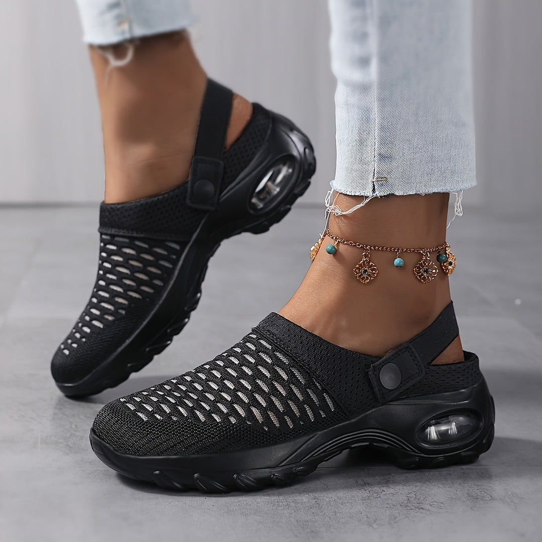 Woman in jeans and a charm anklet walking in black mesh clogs with cutout vamps and a thick air-cushion sole.