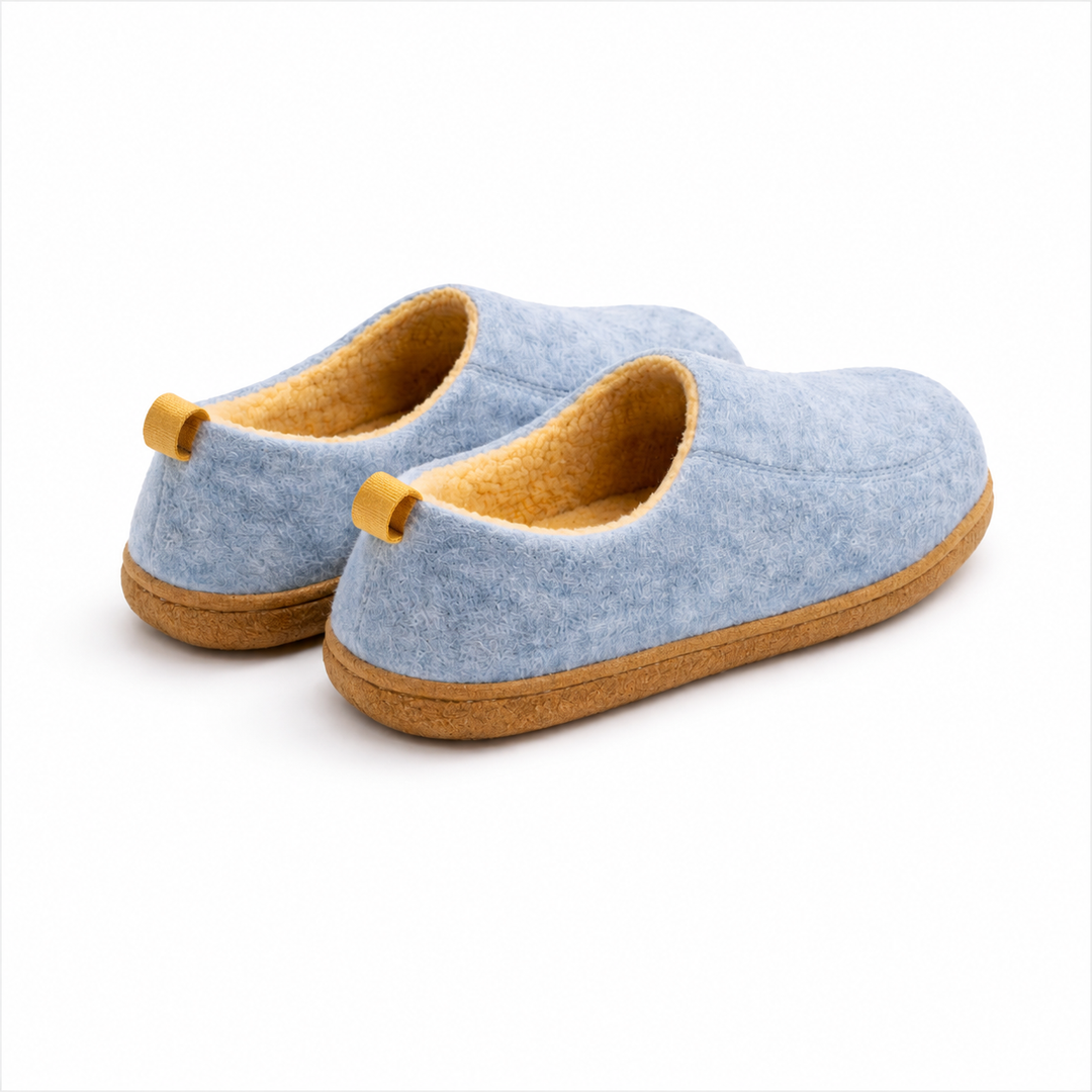 Rear three-quarter detail of light blue slippers showing the yellow heel loops, plush yellow lining and flat tan sole.
