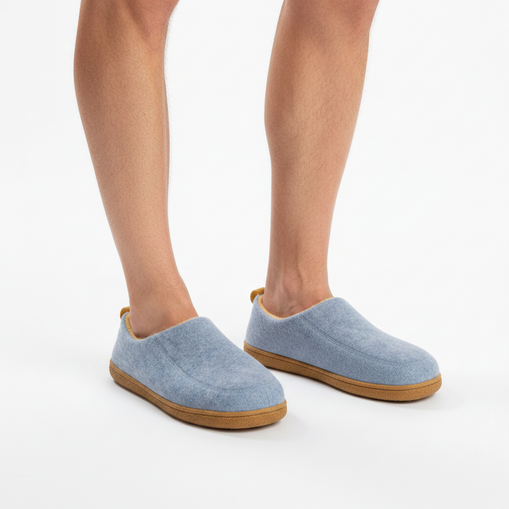 Man's legs wearing light blue felt slippers with tan soles, seen from the front.
