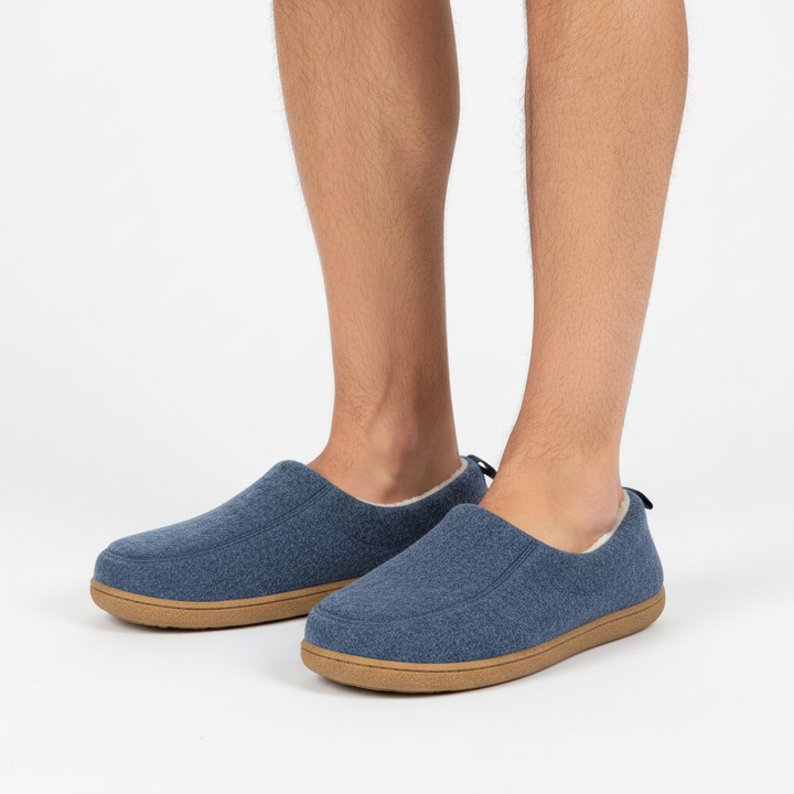 Man's legs wearing navy blue felt slippers with tan soles and a cream fleece collar.