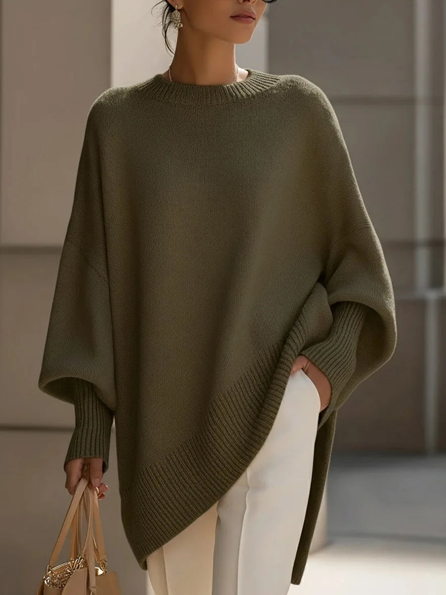 Model wearing the olive green oversized sweater with ribbed cuffs and hem, white pants, holding a tan bag 7