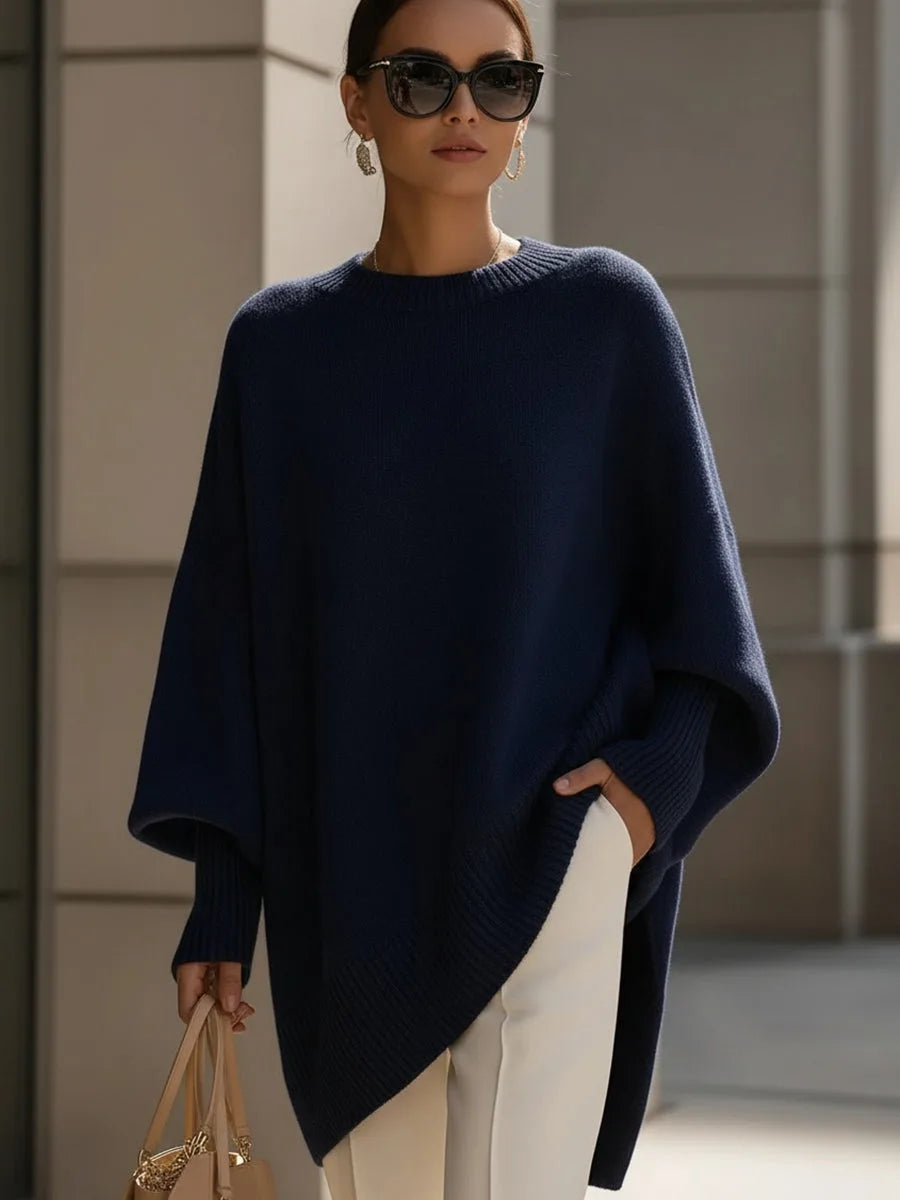 Model wearing the navy blue oversized sweater with sunglasses, white pants and a tan handbag 8