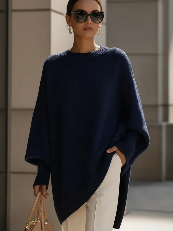 Model wearing the navy blue oversized sweater with sunglasses, white pants and a tan handbag 8