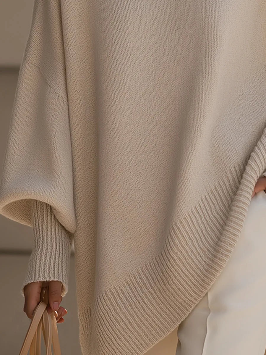 Close-up of the beige sweater's wide ribbed asymmetric hem and ribbed cuff on a hand holding a bag 3