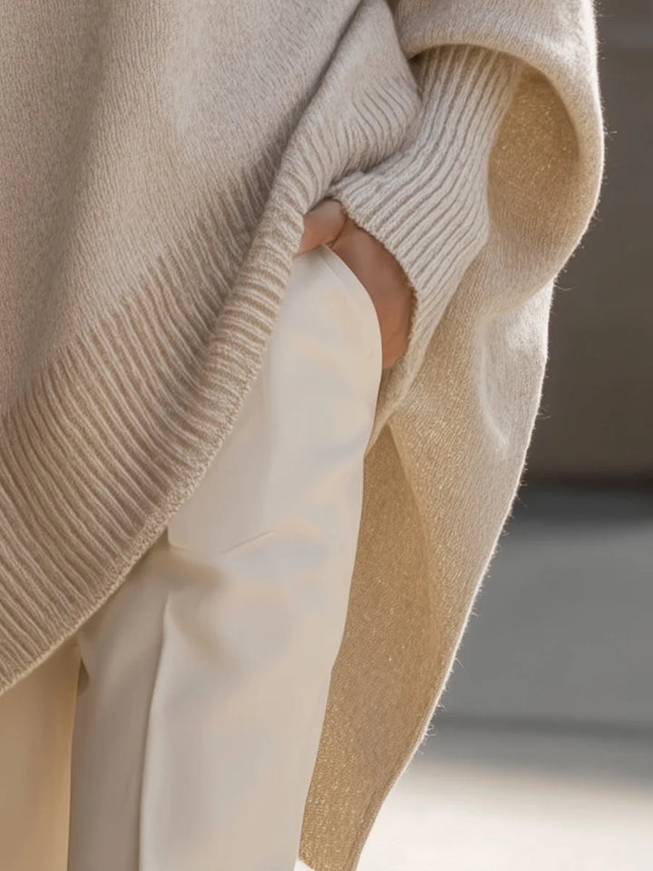 Detail of the beige sweater's side slit, ribbed hem and cuff, with a hand tucked in a white pants pocket 5