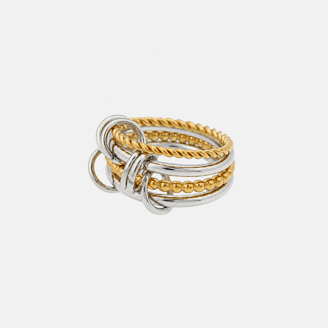 Three-quarter view of a stacked ring combining smooth silver bands, a twisted gold band, a beaded gold band and small interlocking silver loops. 1