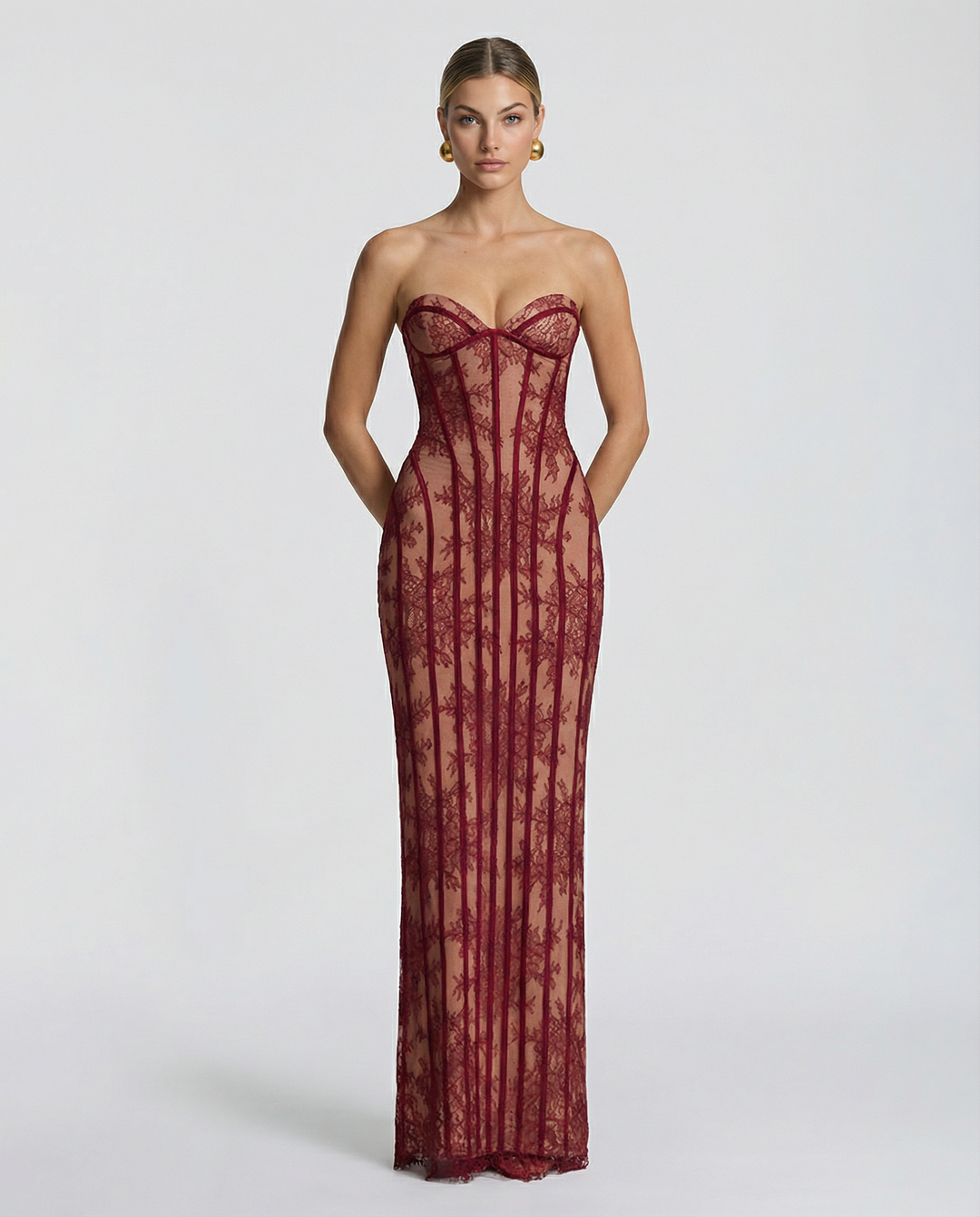 Model faces the camera in a red strapless lace maxi dress with sweetheart bustier neckline and vertical corset boning.