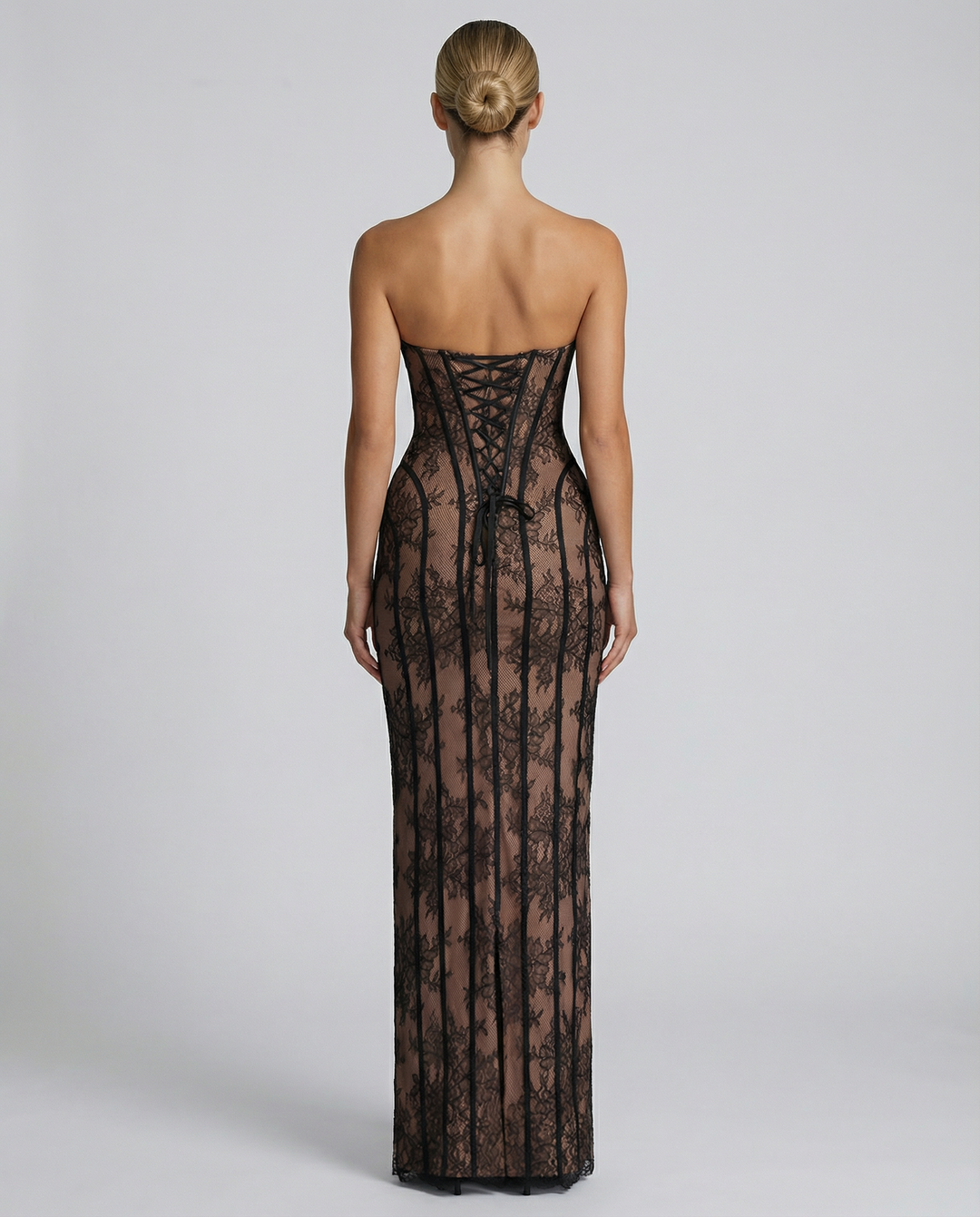 Back view of the black lace dress showing the lace-up corset back with a long tie and a slit at the hem.