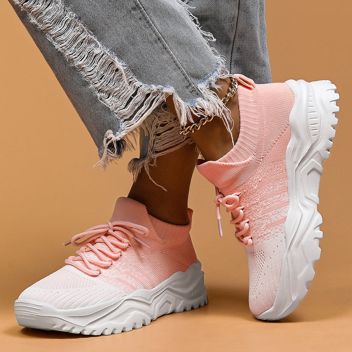 Pink and white gradient knit sneakers worn with ripped gray jeans, front view.