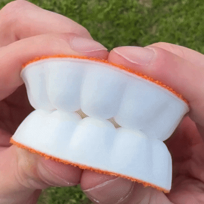 Hands bending a white cushioned insole, showing its soft, flexible foam with orange fabric edges.