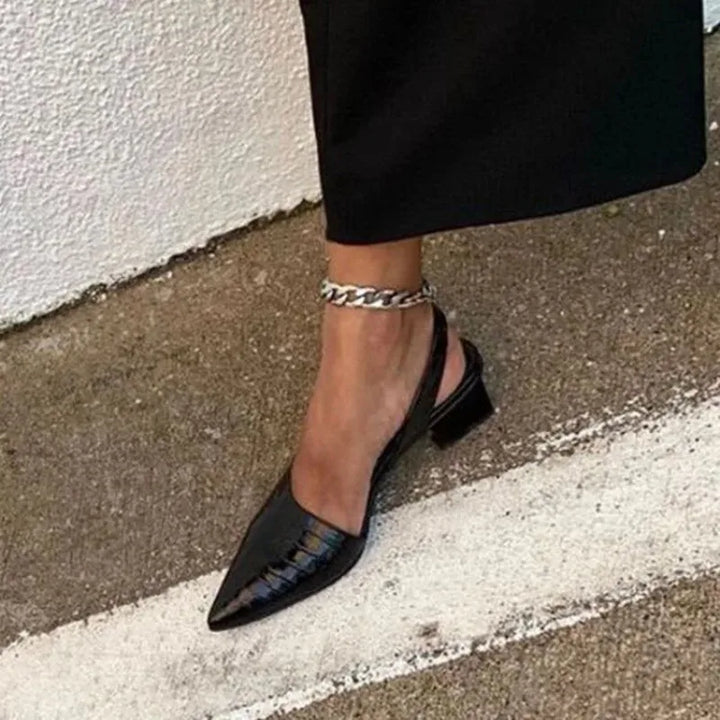 Black croc-embossed slingback worn on a foot with a silver chain anklet and black trousers 1
