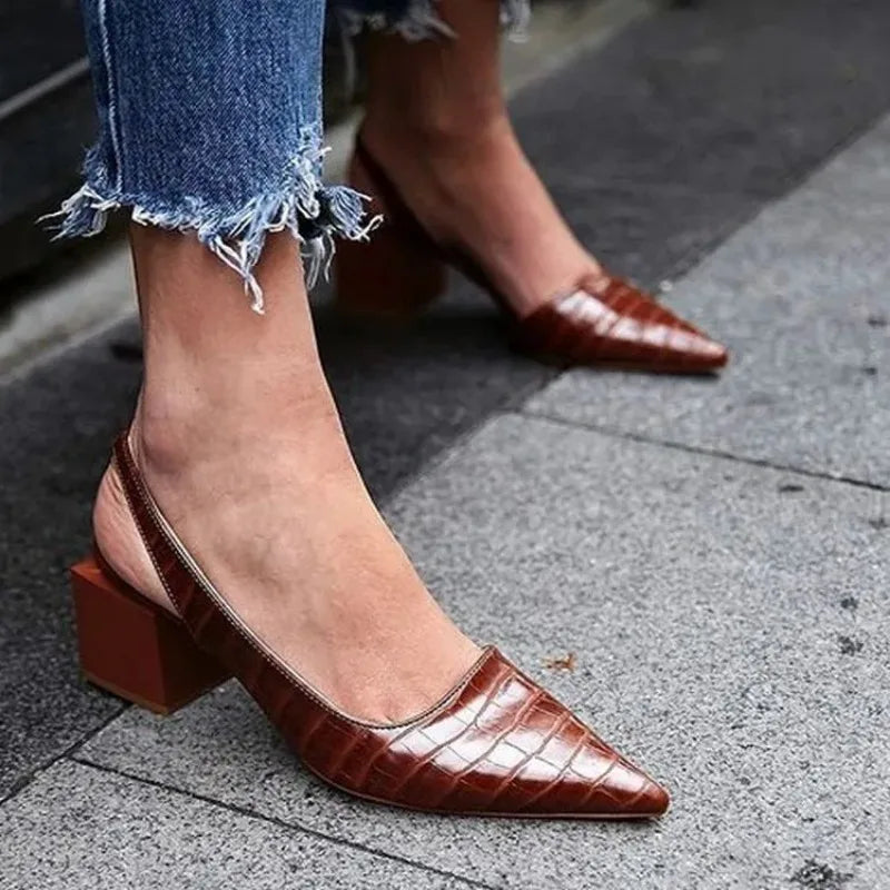 Brown croc-embossed slingback sandals worn with frayed-hem jeans on a paved sidewalk 2