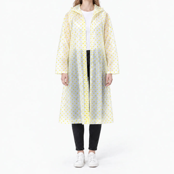 Front view of a woman in a translucent long raincoat with yellow polka dots, snap front open over a white tee and black jeans. 11