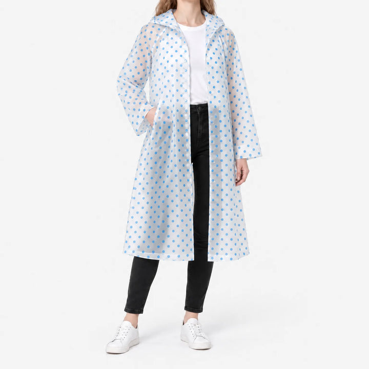 Woman in a translucent long raincoat with blue polka dots, hood down, one hand in a pocket, snap front open over a white tee. 2