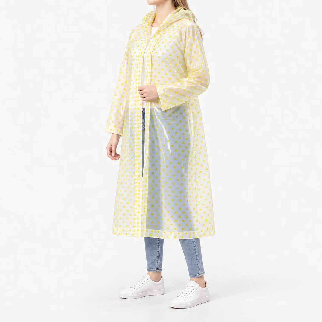 Three-quarter side view of a woman in a translucent long raincoat with yellow polka dots, hood down and front open over jeans. 5