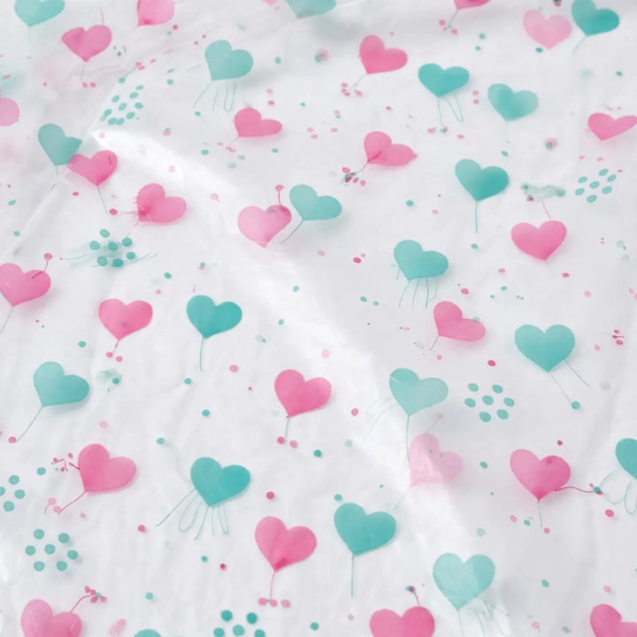 Close-up of the translucent raincoat material printed with pink and teal hearts and small dots, with soft creases catching the light. 6