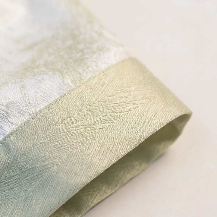 Close-up of a green cuff with herringbone texture and stitching against the glossy marbled white fabric. 5