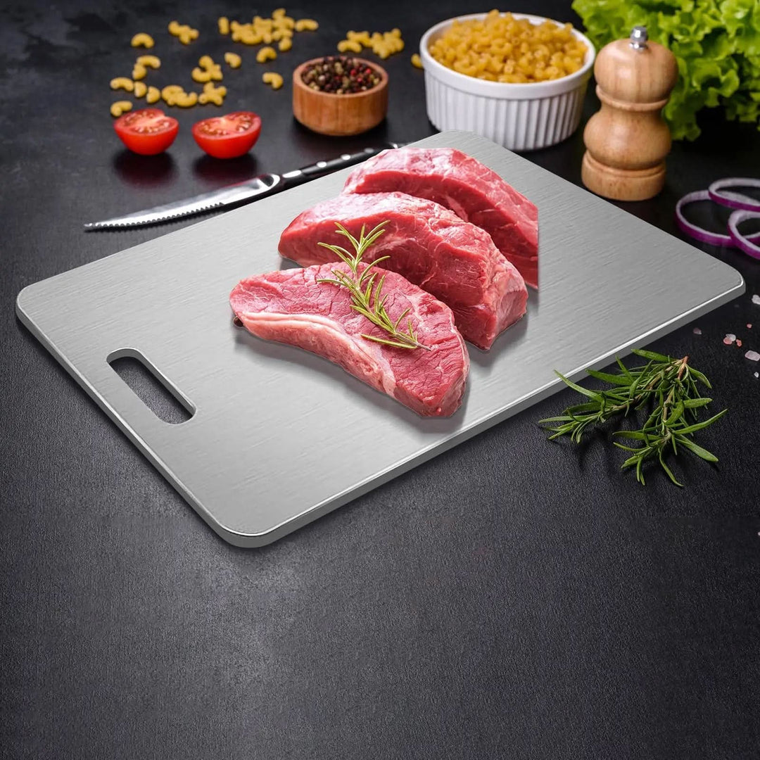 Metal board on a dark surface holding three raw beef cuts with a rosemary sprig, surrounded by pasta, peppercorns and a wooden grinder. 4