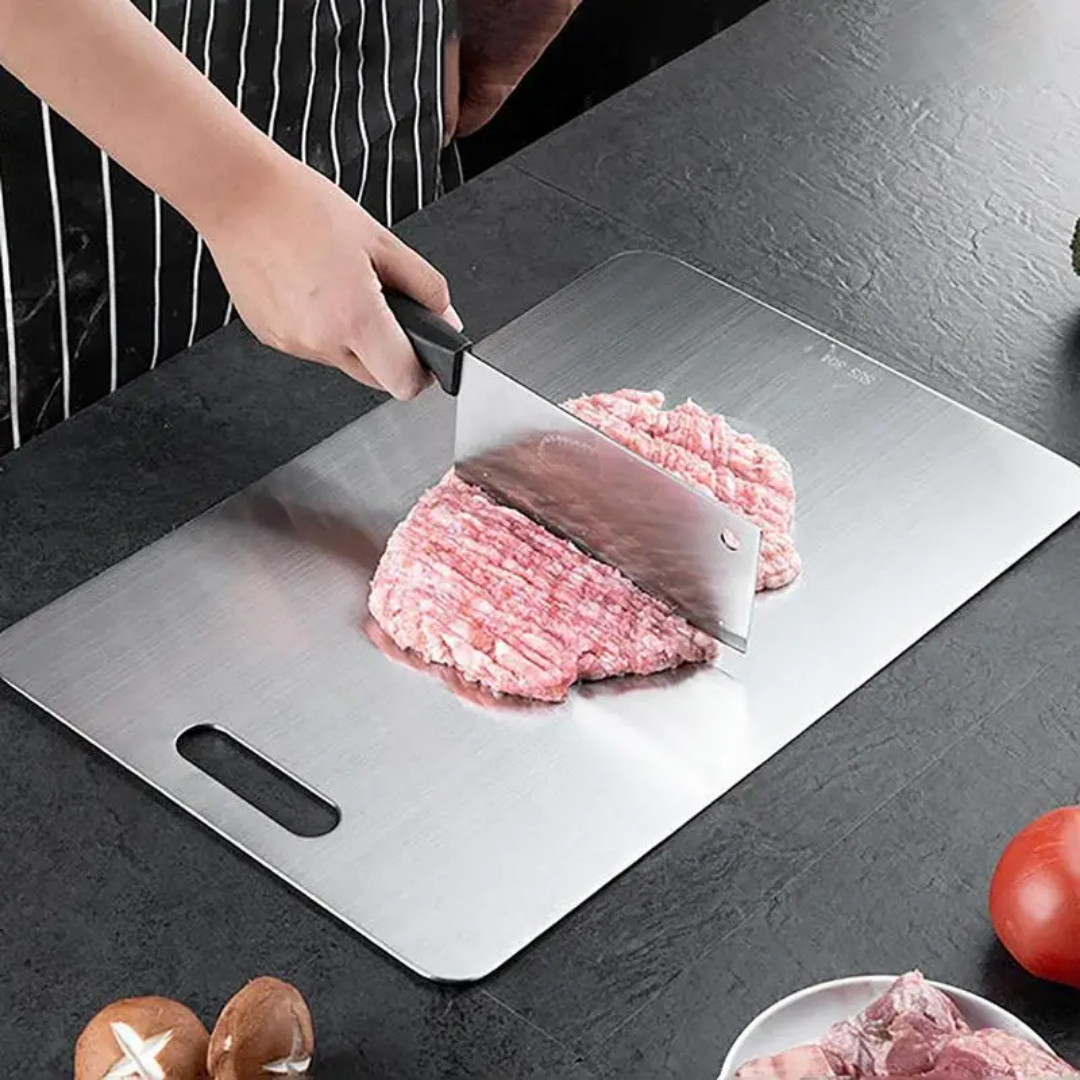 Cook chopping ground meat with a cleaver on the large steel board, shown on a dark slate counter with mushrooms and a tomato. 6