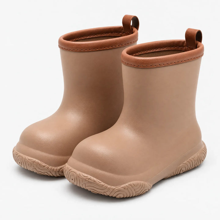 Pair of tan rain boots with brown trim and pull loops, angled three-quarter view on a white background. 2