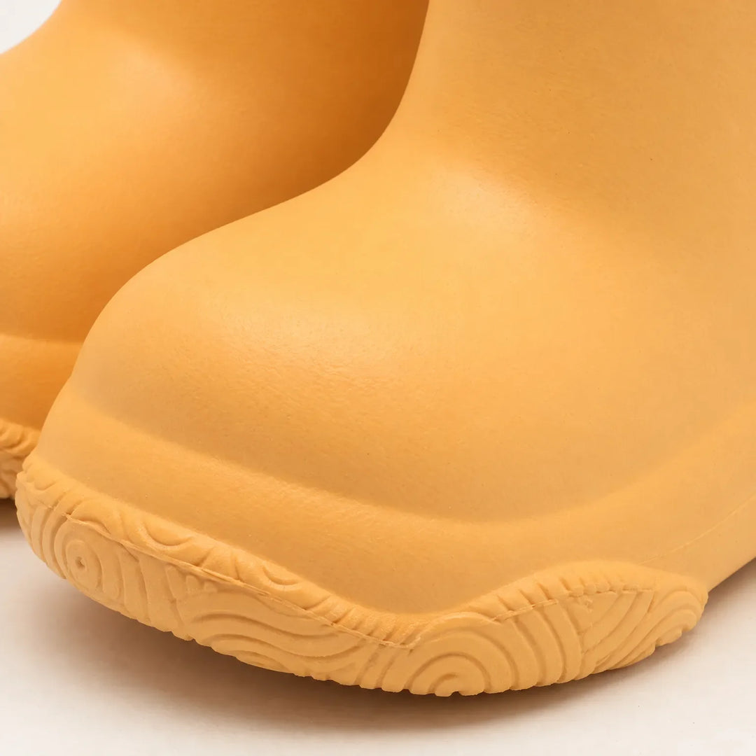 Close-up of an orange boot toe showing the smooth rounded shape and the swirl-patterned tread along the sole edge. 6