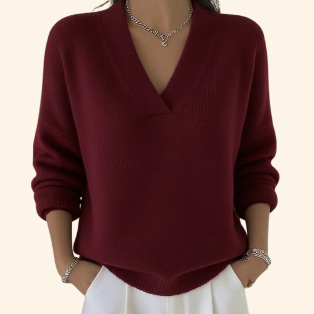 Model wearing the knit V-neck sweater in burgundy with white trousers and silver jewelry.