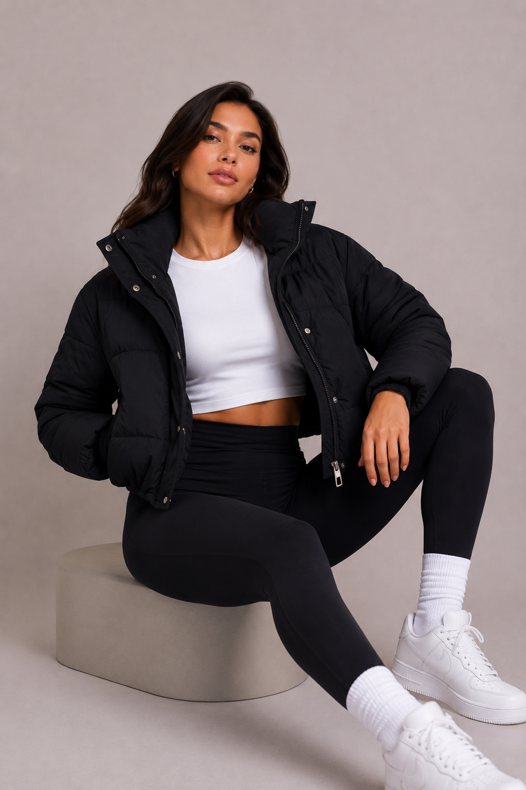 Black cropped puffer jacket another view worn open over a white crop top while seated.