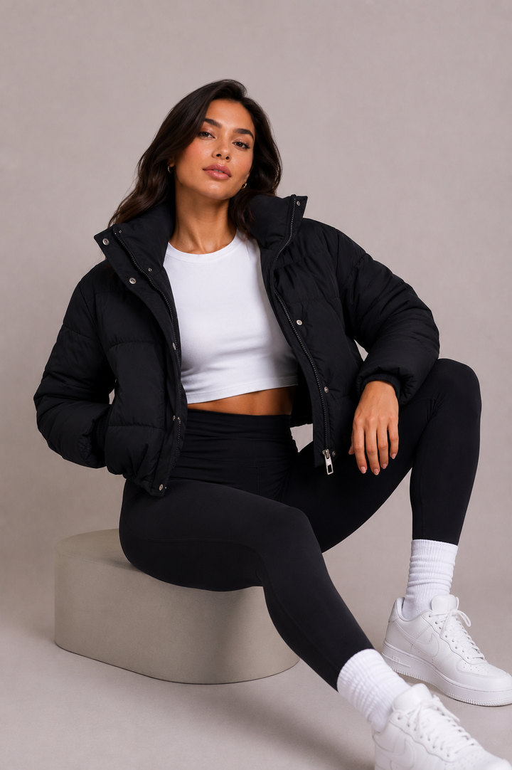 Black cropped puffer jacket another view worn open over a white crop top while seated.