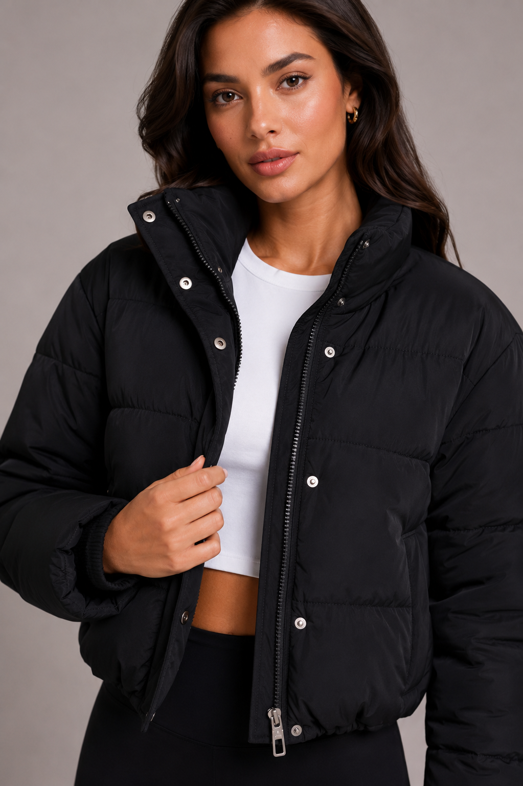 Black quilted jacket with fitted hood, high collar and snap placket shown open over a white crop top.