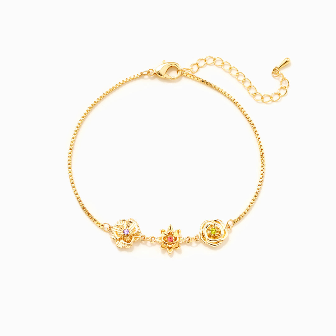 Gold-tone birth flower bracelet with three flower charms and an extender chain, laid flat on white.