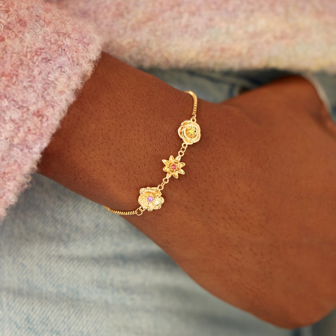 Close-up of a wrist wearing the gold birth flower bracelet with a pink sleeve.