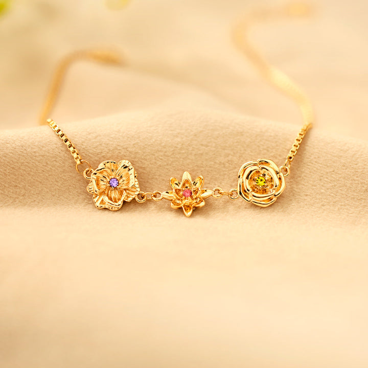Gold birth flower bracelet with three flower charms and purple, pink and yellow-green stones.