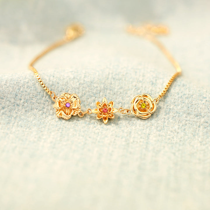 Gold birth flower bracelet with purple, red and yellow stones on pale blue fabric.