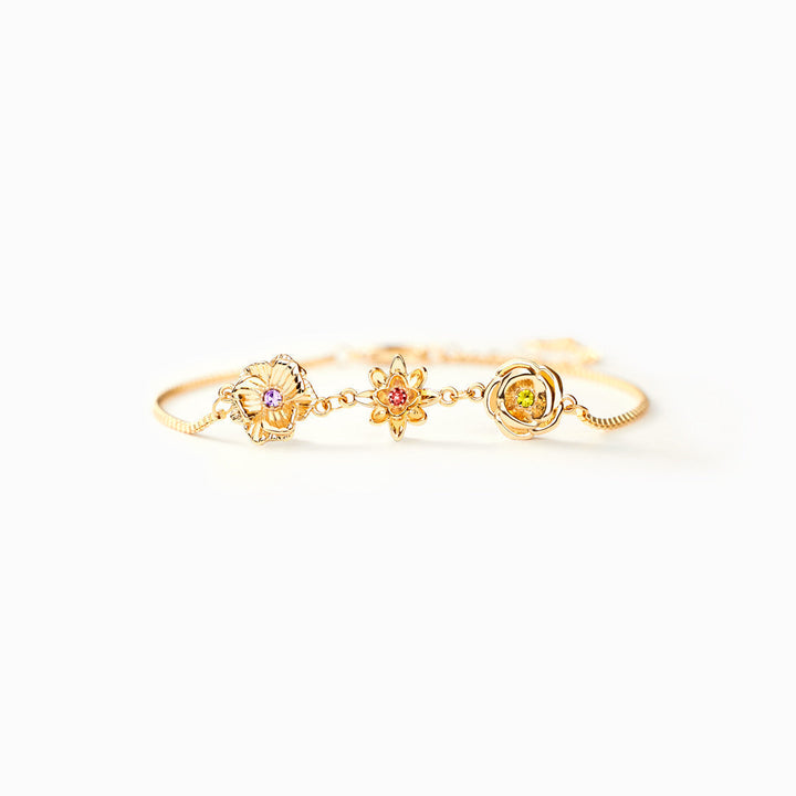 Gold-tone birth flower bracelet with three flower charms, shown from the front on white.