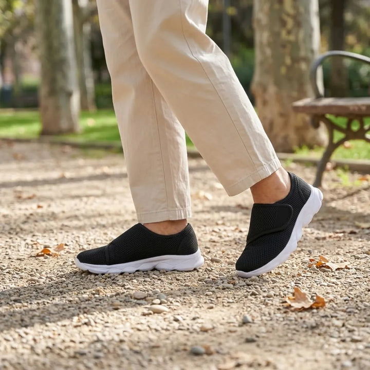 Person walking on a gravel path in black mesh strap shoes with white soles and loose beige pants 20