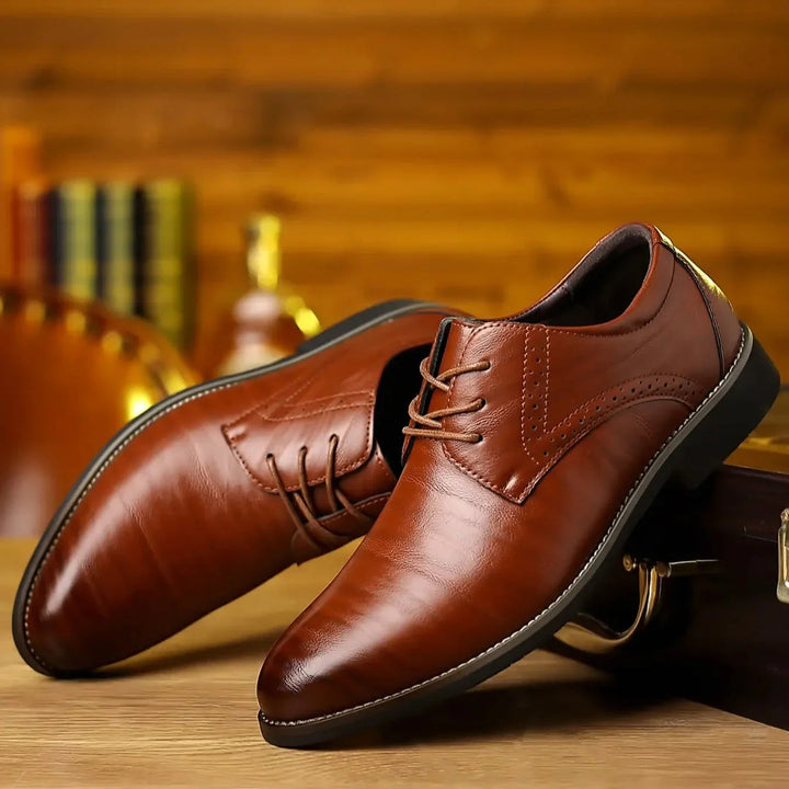 Pair of brown faux-leather lace-up shoes with brogue detailing, one resting on the other, on a wooden table.