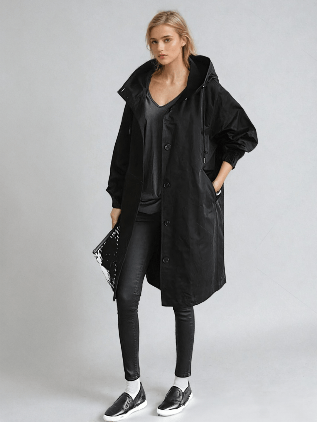Model in the black version of the hooded coat, worn open with skinny jeans, slip-on sneakers and a clutch 2