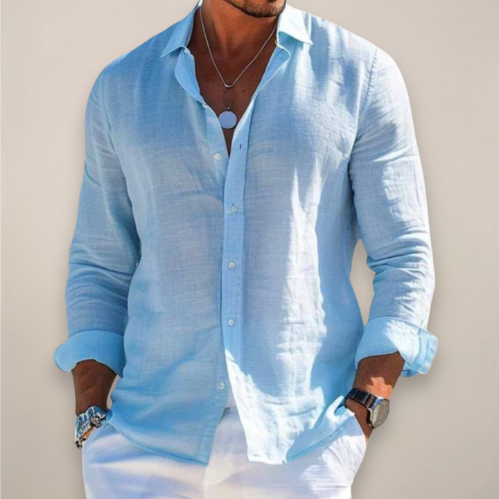 Man wearing the light blue long-sleeved button-front shirt with rolled sleeves and hands in white pants pockets.