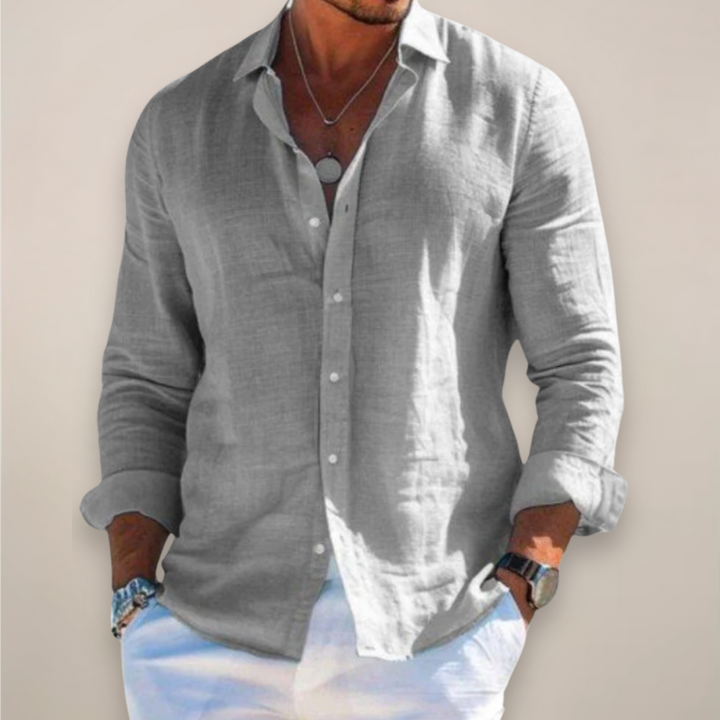 Man wearing the blue long-sleeved button-front shirt with sleeves rolled up and hands in white pants pockets.