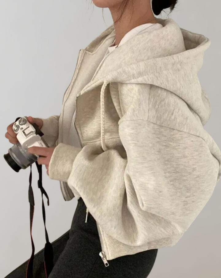 Side view of the light heather gray hoodie on a model holding a camera, showing the voluminous sleeve and large hood.