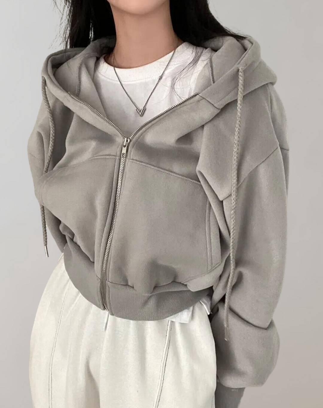 Front view of the gray hoodie zipped partway over a white tee, showing the ribbed hem, seamed front panels and braided drawstrings.