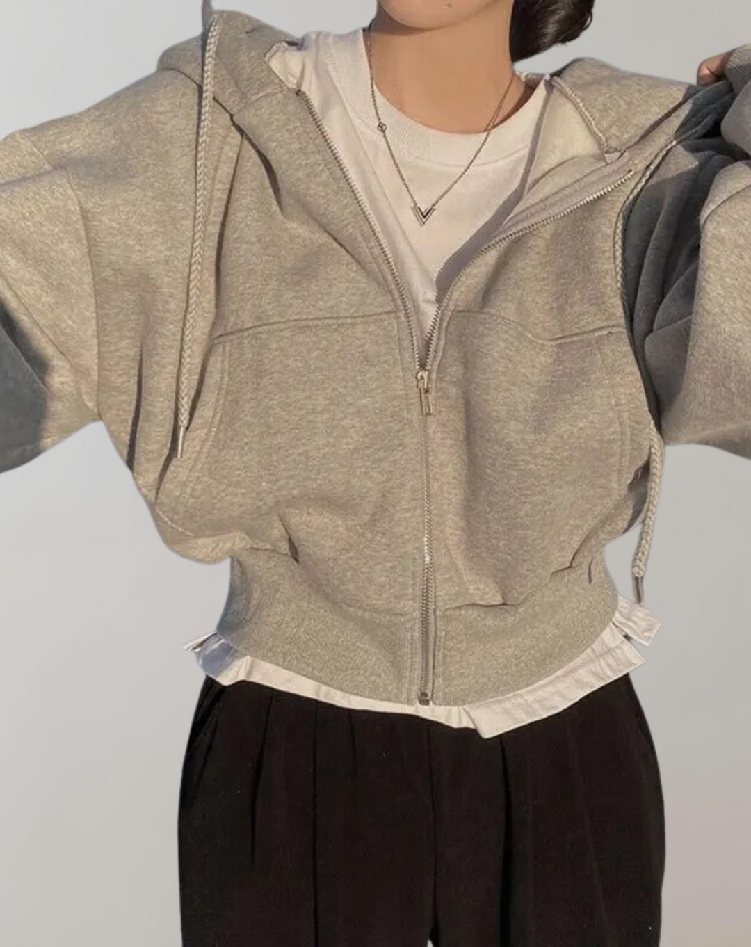 Heather gray hoodie worn unzipped over a white tee and black trousers, with arms raised to show the relaxed cropped fit.