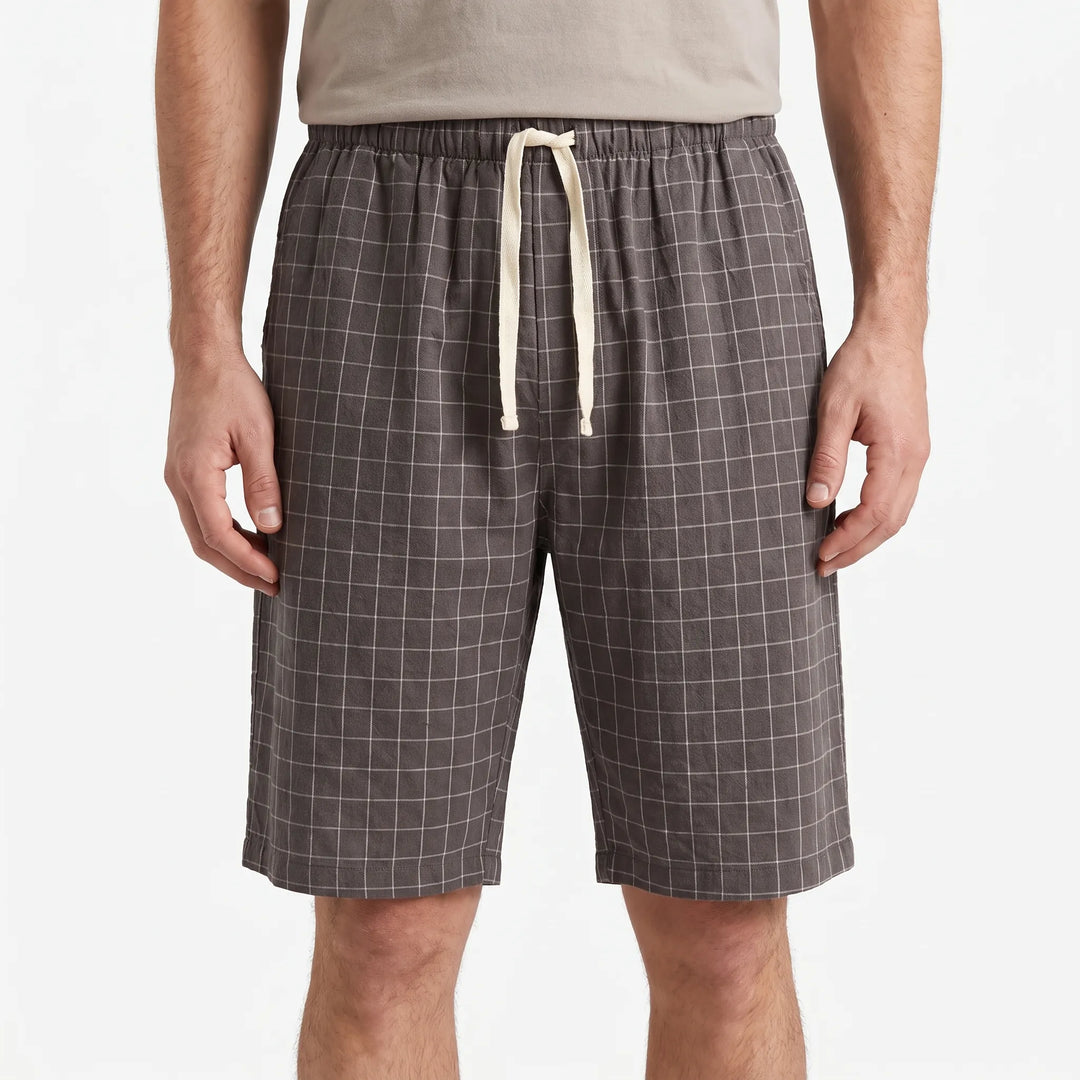 Front view of gray windowpane-check shorts with elastic waist and cream drawstring on a model against a plain white background. 2