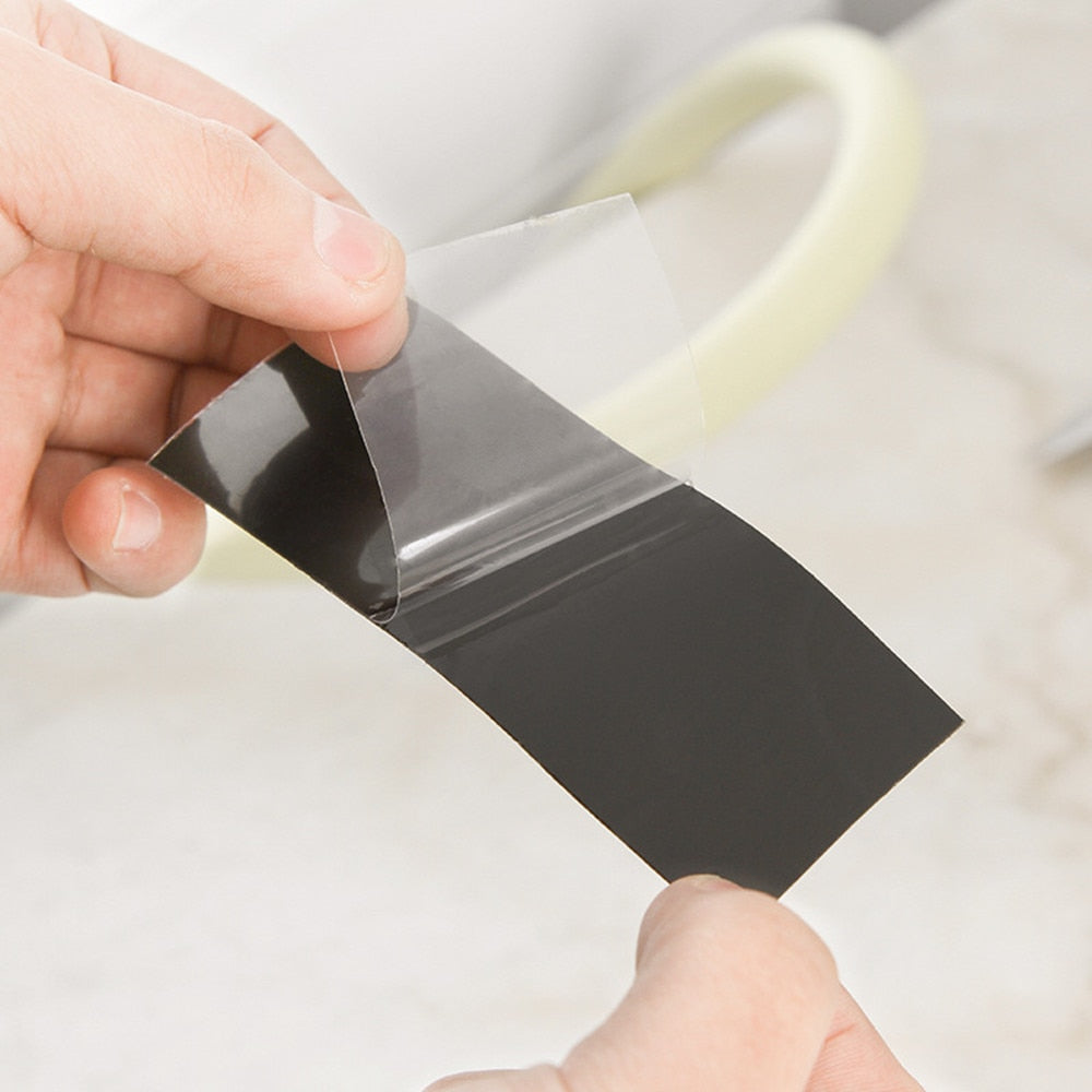 Fingers peel the clear protective film from a short black strip of tape.