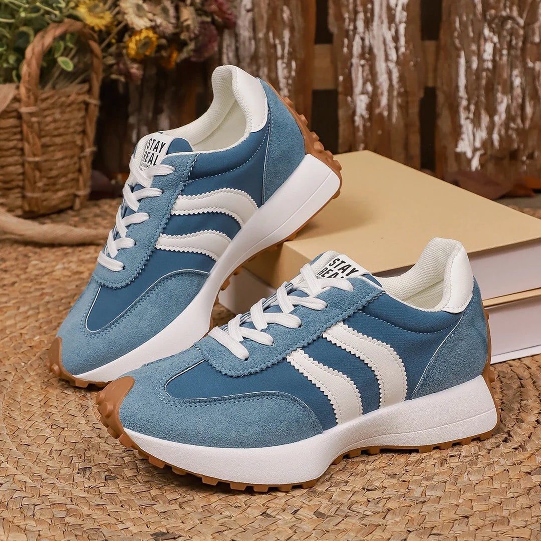 Pair of blue suede trainers with white stripes and gum soles, displayed on a woven mat beside books 5
