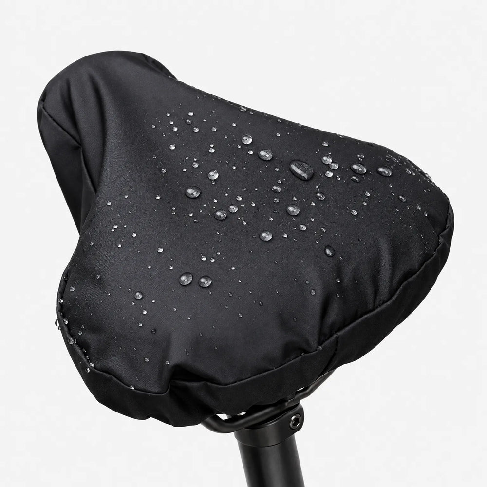 Close-up of the black cover on a saddle against a white background, with water droplets beading on the surface. 2