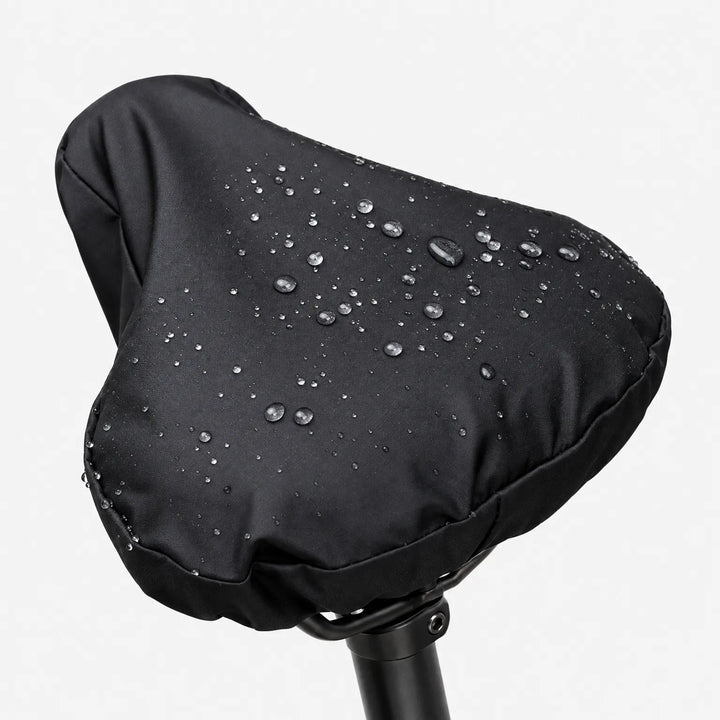 Close-up of the black cover on a saddle against a white background, with water droplets beading on the surface. 2