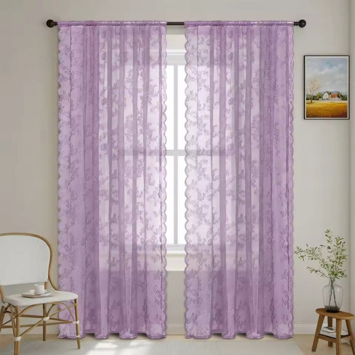 Pair of lilac purple floral lace panels hang from a dark rod at a window, with a white chair and plant nearby.