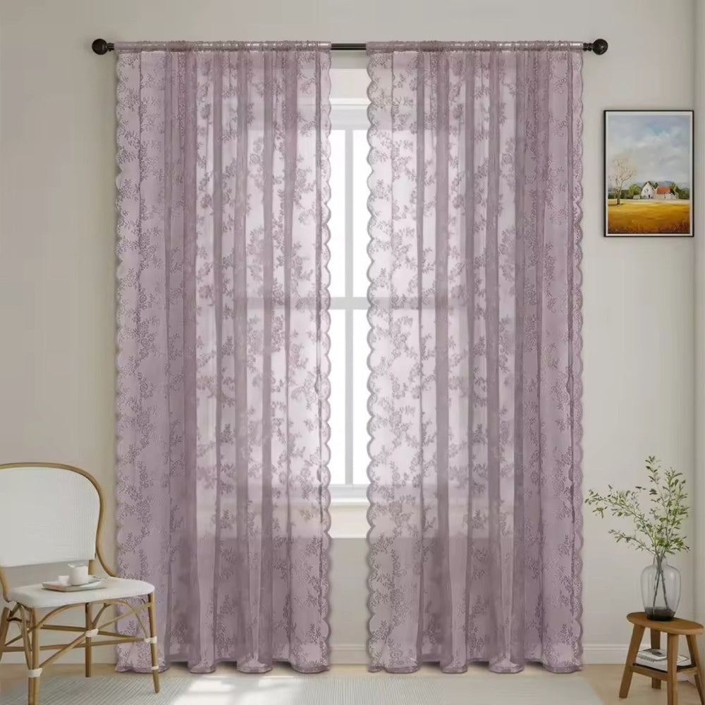 Pair of muted mauve floral lace panels with scalloped edges hang from a dark rod in a softly lit room.