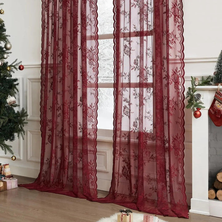 Burgundy floral lace panels with scalloped edges hang at a snowy window, styled in a room decorated for Christmas.